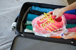 woman placing tennis shoes in a shower cap in luggage