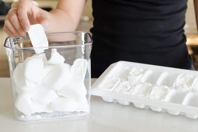 a person putting homemade dishwasher tabs from an ice cube tray into a clear container 