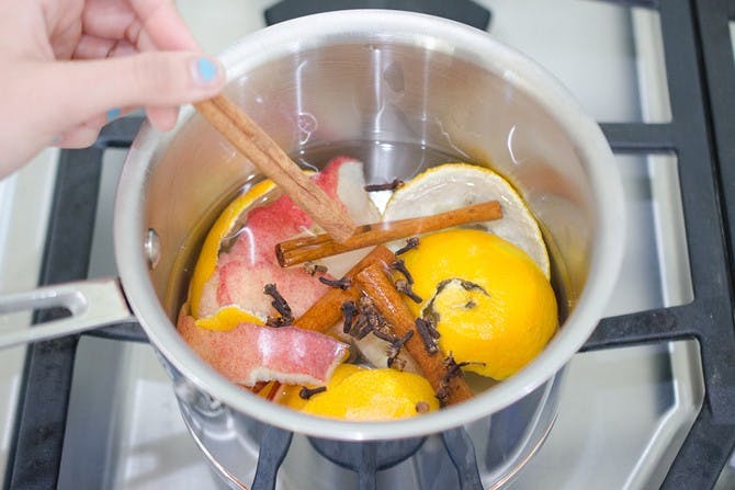 A woman placing a cinnamon stick into a pot with cloves, lemon peels and apple peels