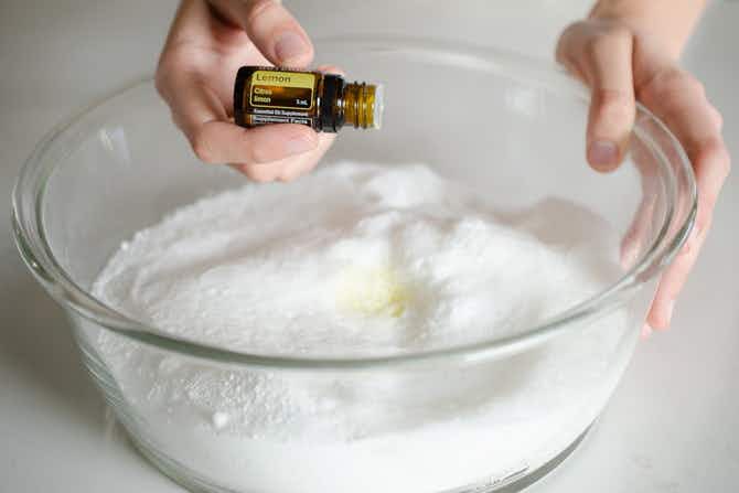 a person adding lemon essential oil to a bowl of dishwashing detergent 