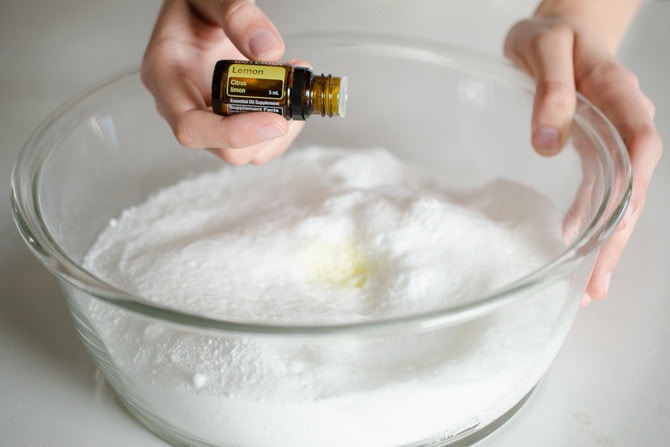 a person adding lemon essential oil to a bowl of dishwashing detergent 