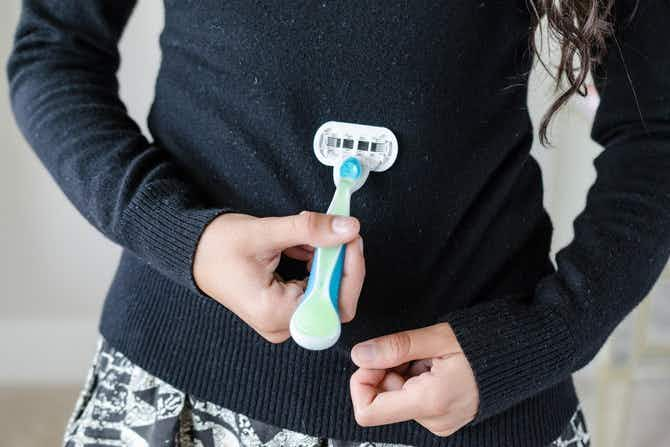 A person using a razor to remove pills from a sweater.