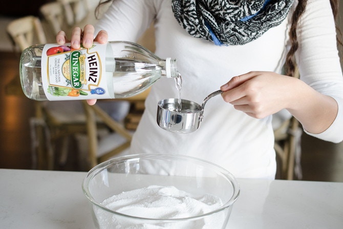 a person pouring vinegar into a measuring cup for make dishwasher tabs