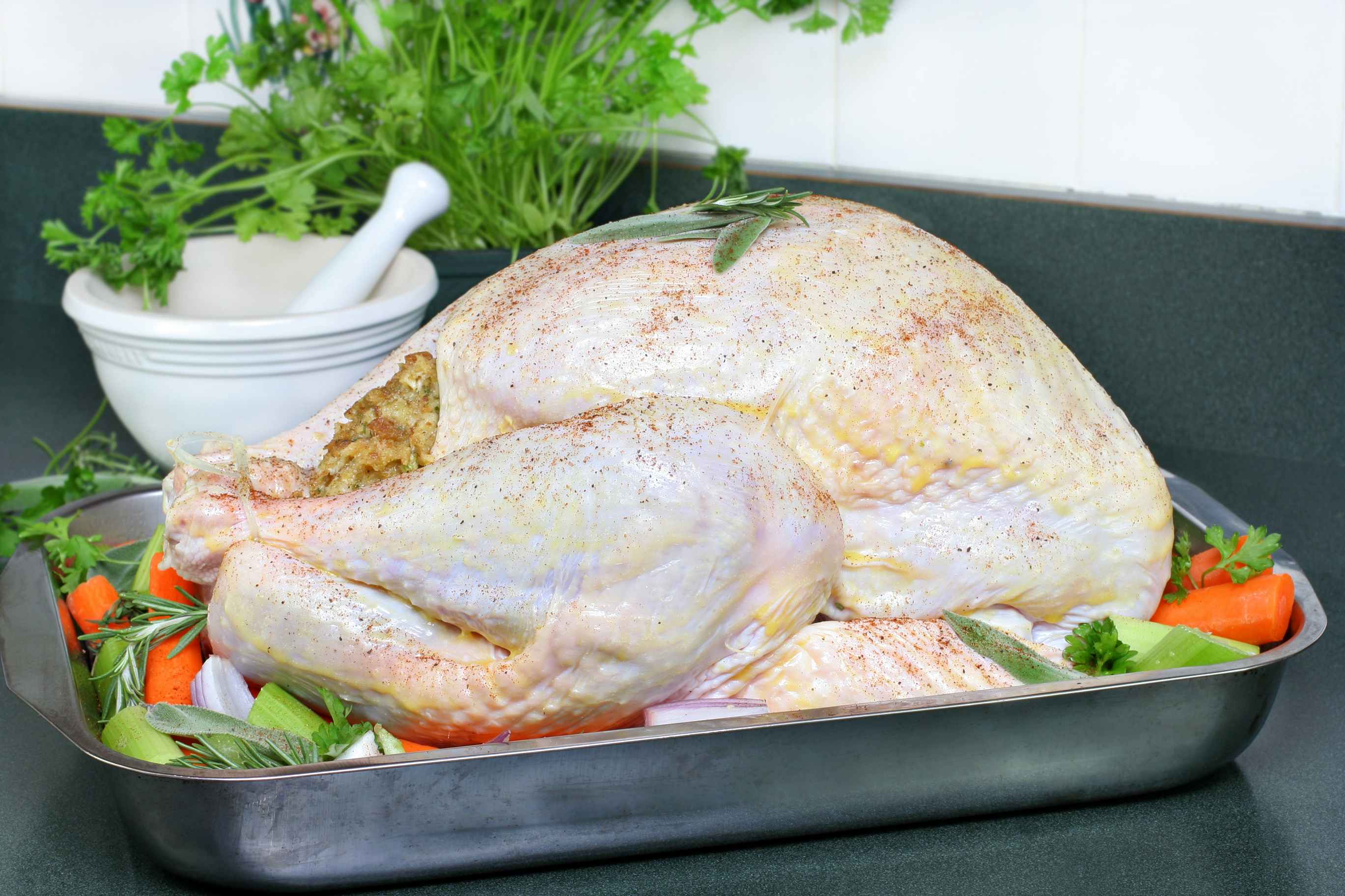 A Thanksgiving turkey in a pan on top of quartered vegetables.