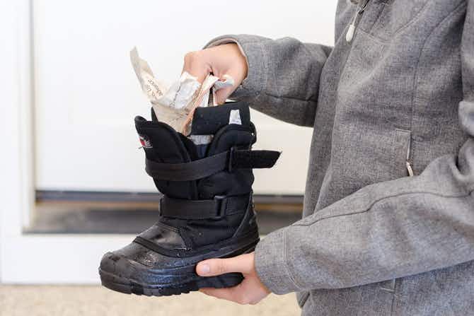 A person stuffing a kids winter boot with newspaper. 