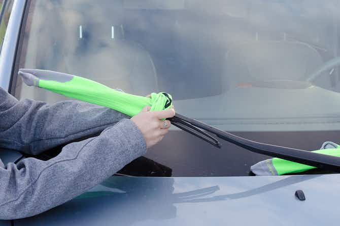 A person putting a sock onto a windshield wiper.