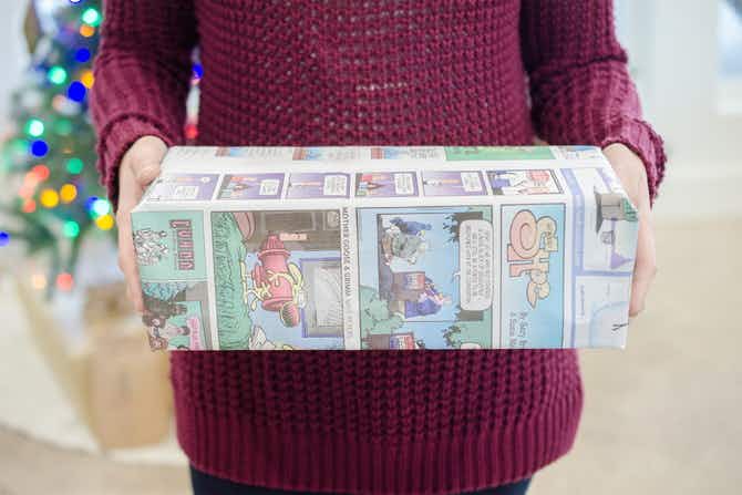 A person holding a box wrapped in newspaper.
