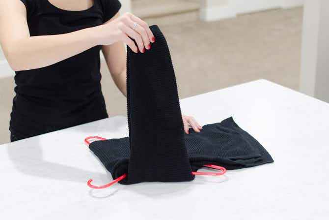 A person folding a sweater over a hanger