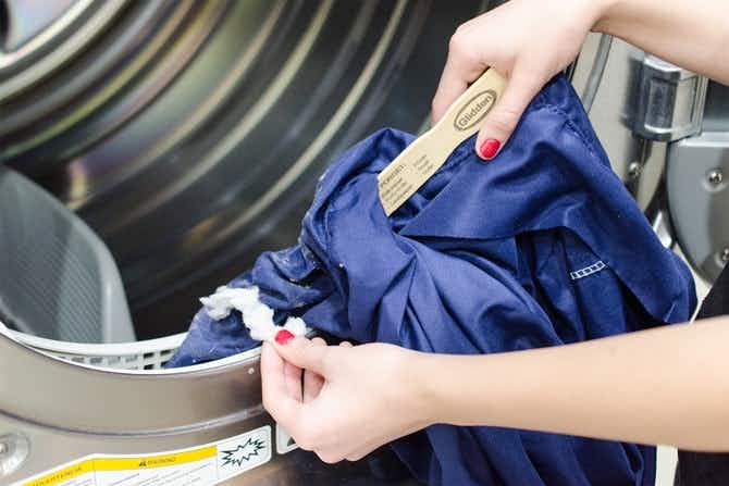 A person using a paint stirring stick and a pillowcase to clean out a dryer's link trap