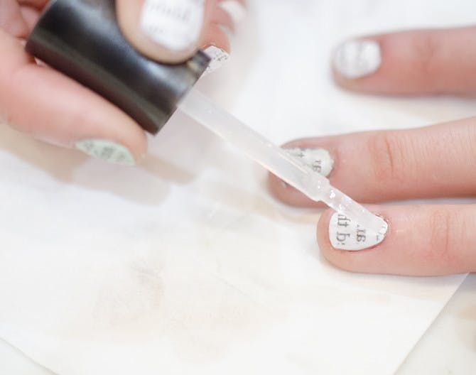 A person painting nails with pieces of newspaper on the nails.