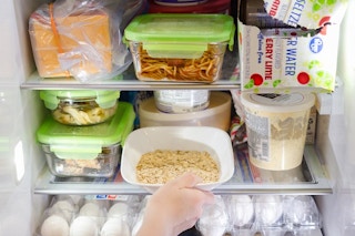 Someone putting a bowl of oats into a full refrigerator