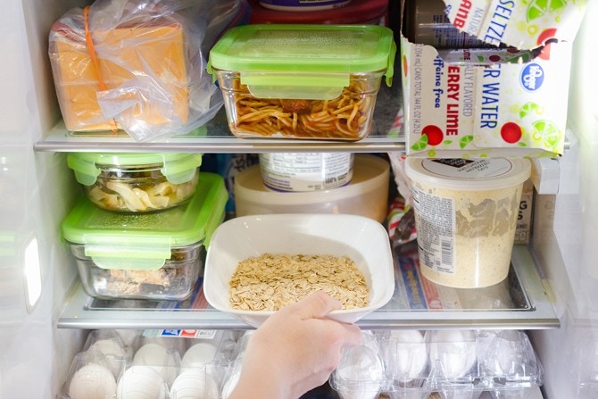 Someone putting a bowl of oats into a full refrigerator