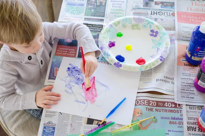 A child painting on a table covered in newspaper.