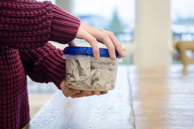 A person holding a plastic container with newspaper in it.