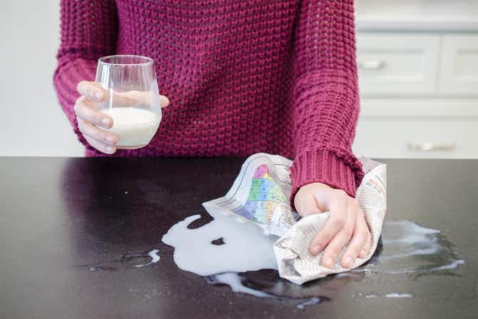 A person wiping up spilled milk on a counter with a newspaper.
