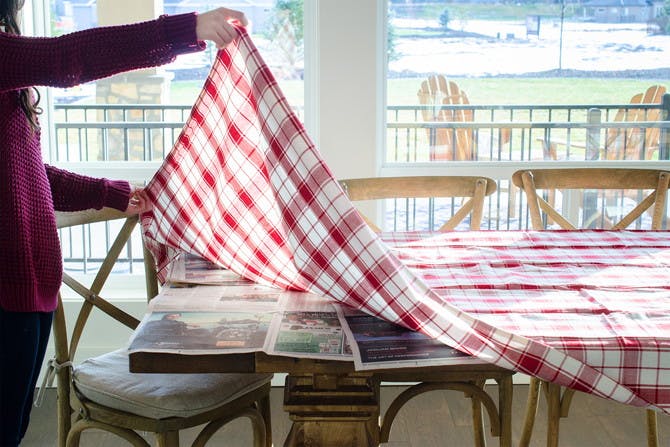 A person holding up a tablecloth above a table with newspaper on it.