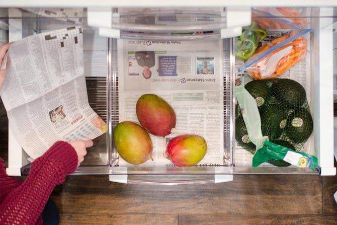 A refrigerator vegetable drawer with newspaper under mangos and avacados.