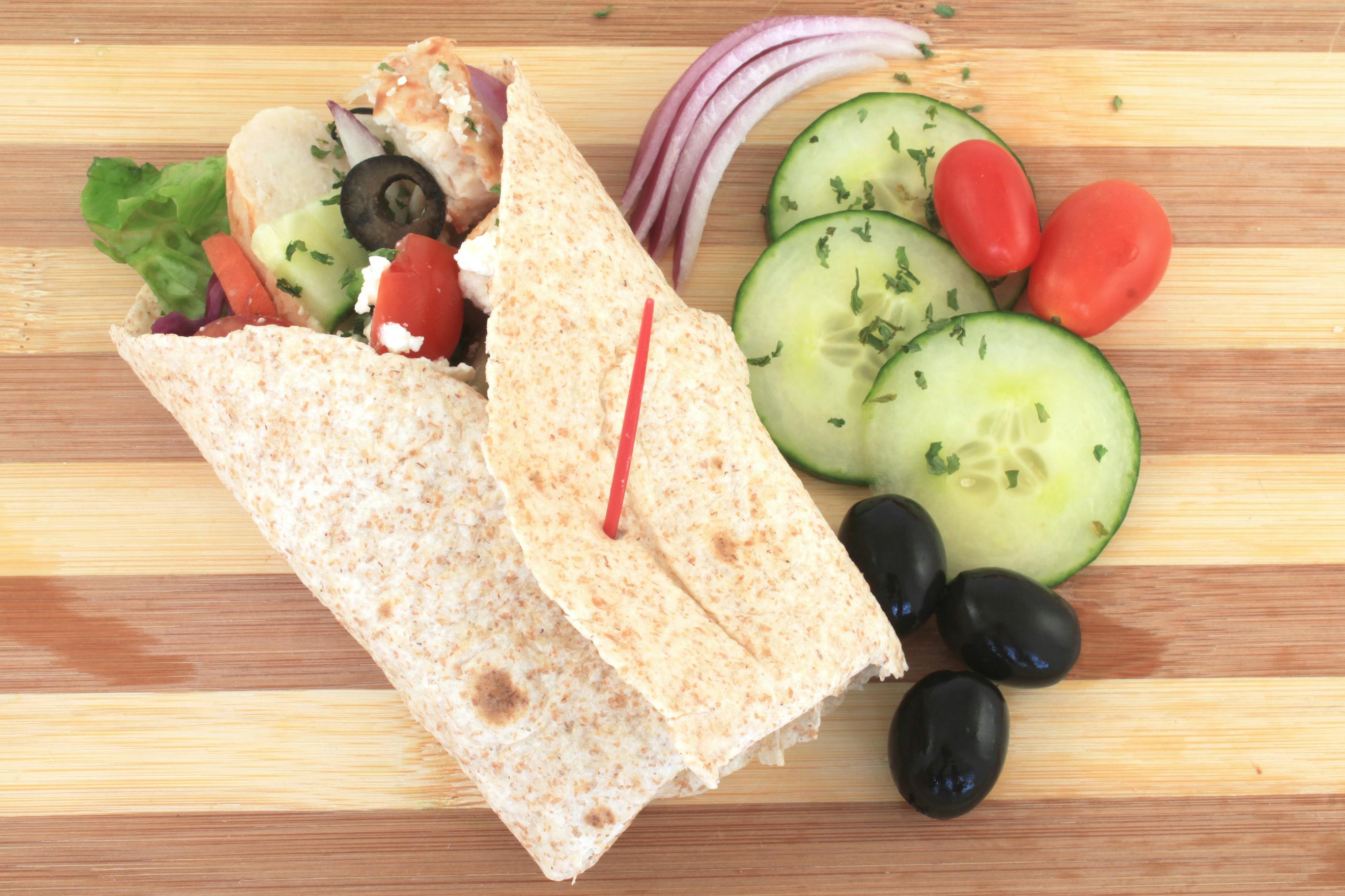 A greek chicken wrap with some ingredients on a wood surface