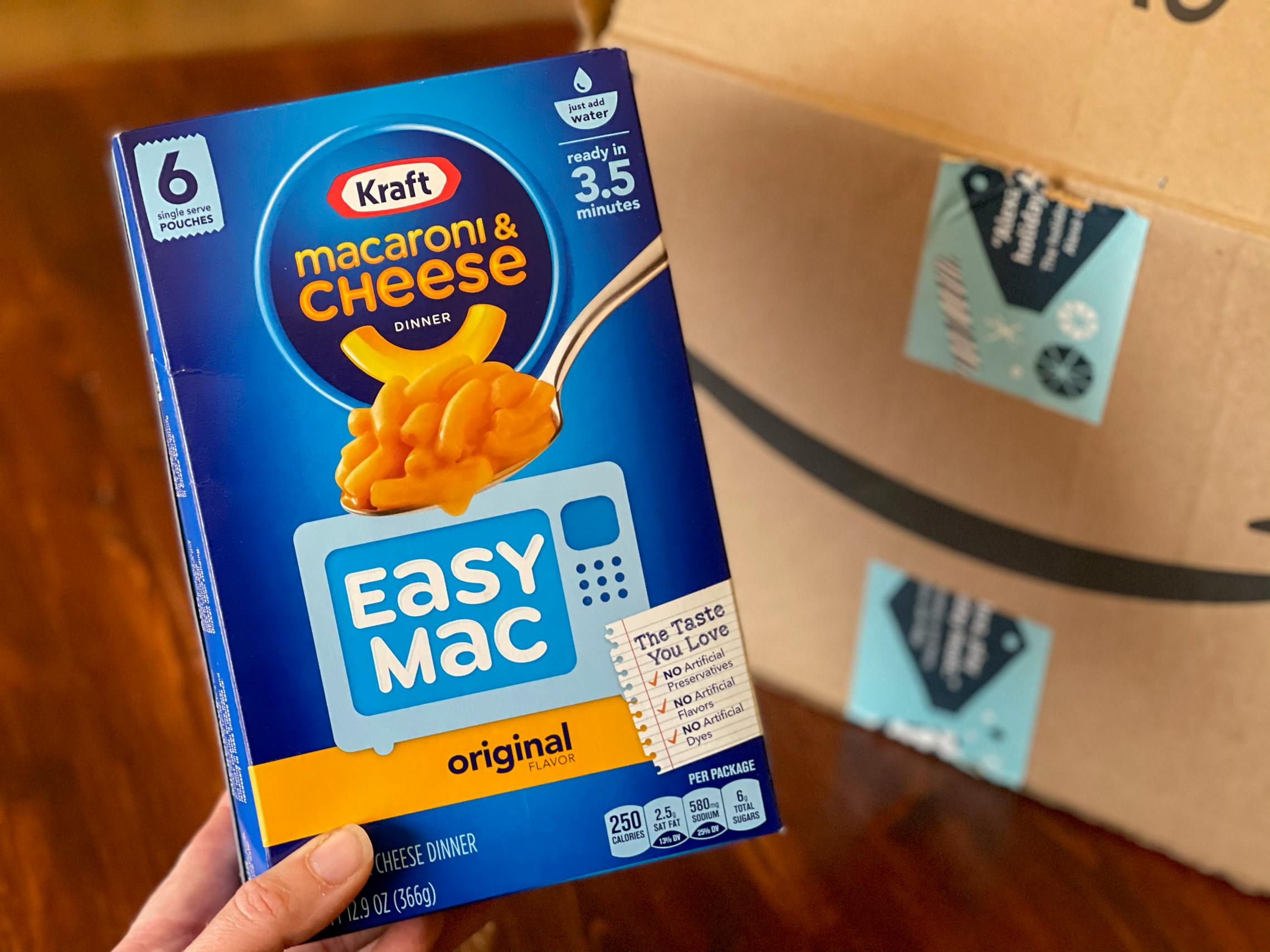 A person holding a box of Macaroni & Cheese Easy Mac in front of an Amazon box.