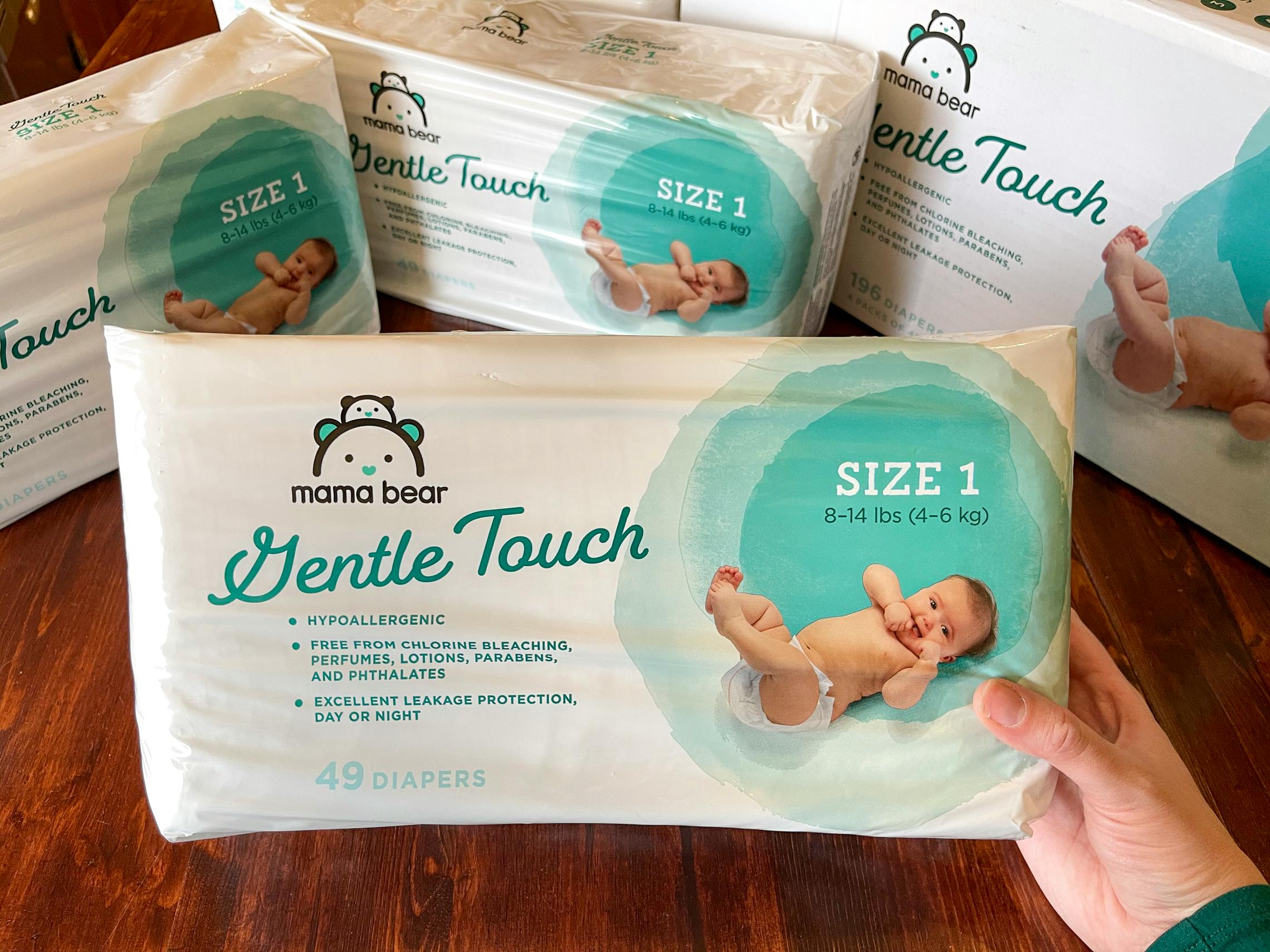 A person holding a pack of Amazon Mama Bear diapers, with other packages in the background.