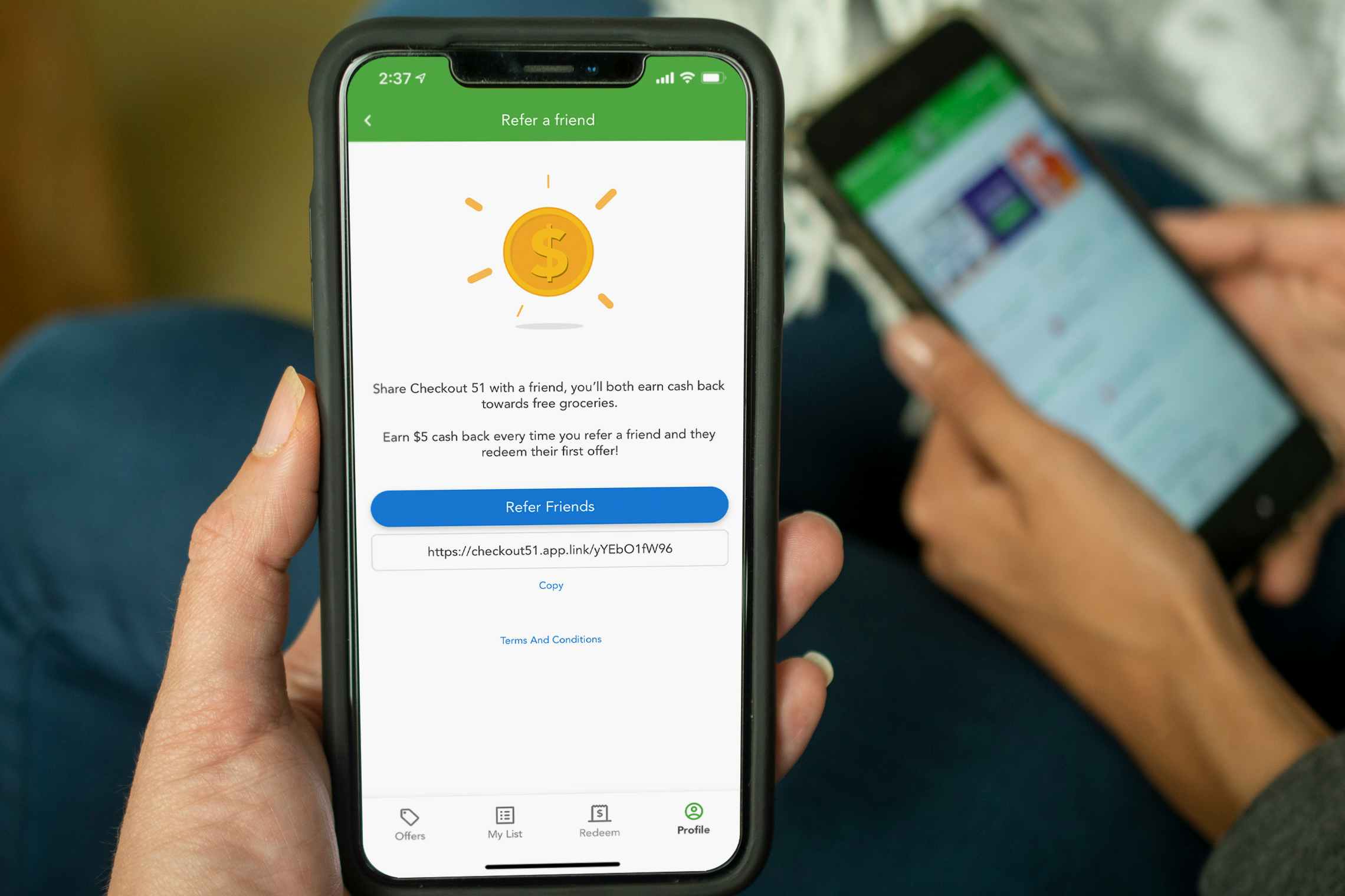 Two cell phones in two peoples hands. One phone displaying the refer a friend page on the Checkout 51 app.
