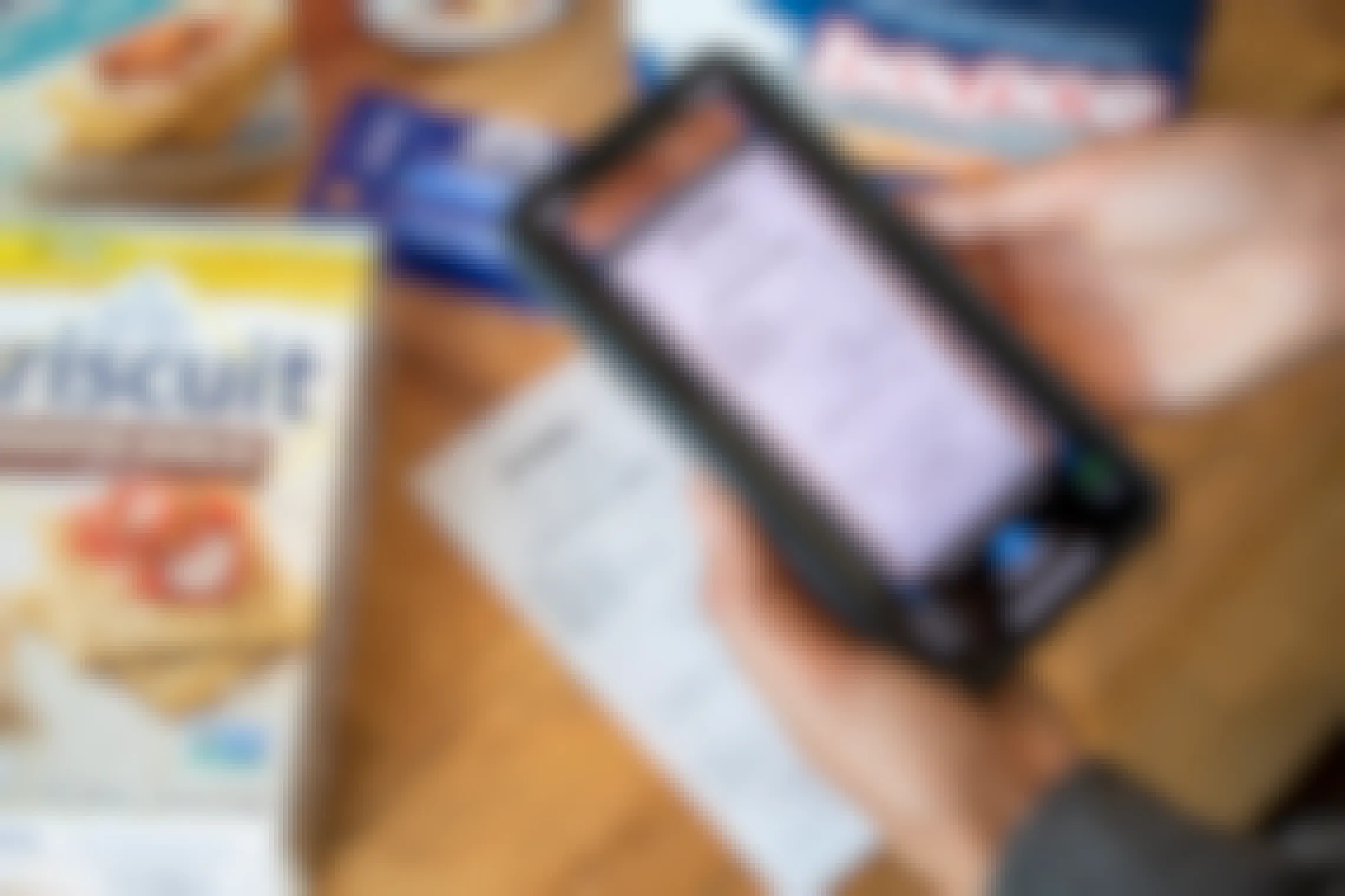 A person taking a photo of a Target receipt through the Checkout51 mobile app's scan feature. On the table next to the receipt are various grocery items including Triscuit crackers and Bounce dryer sheets.