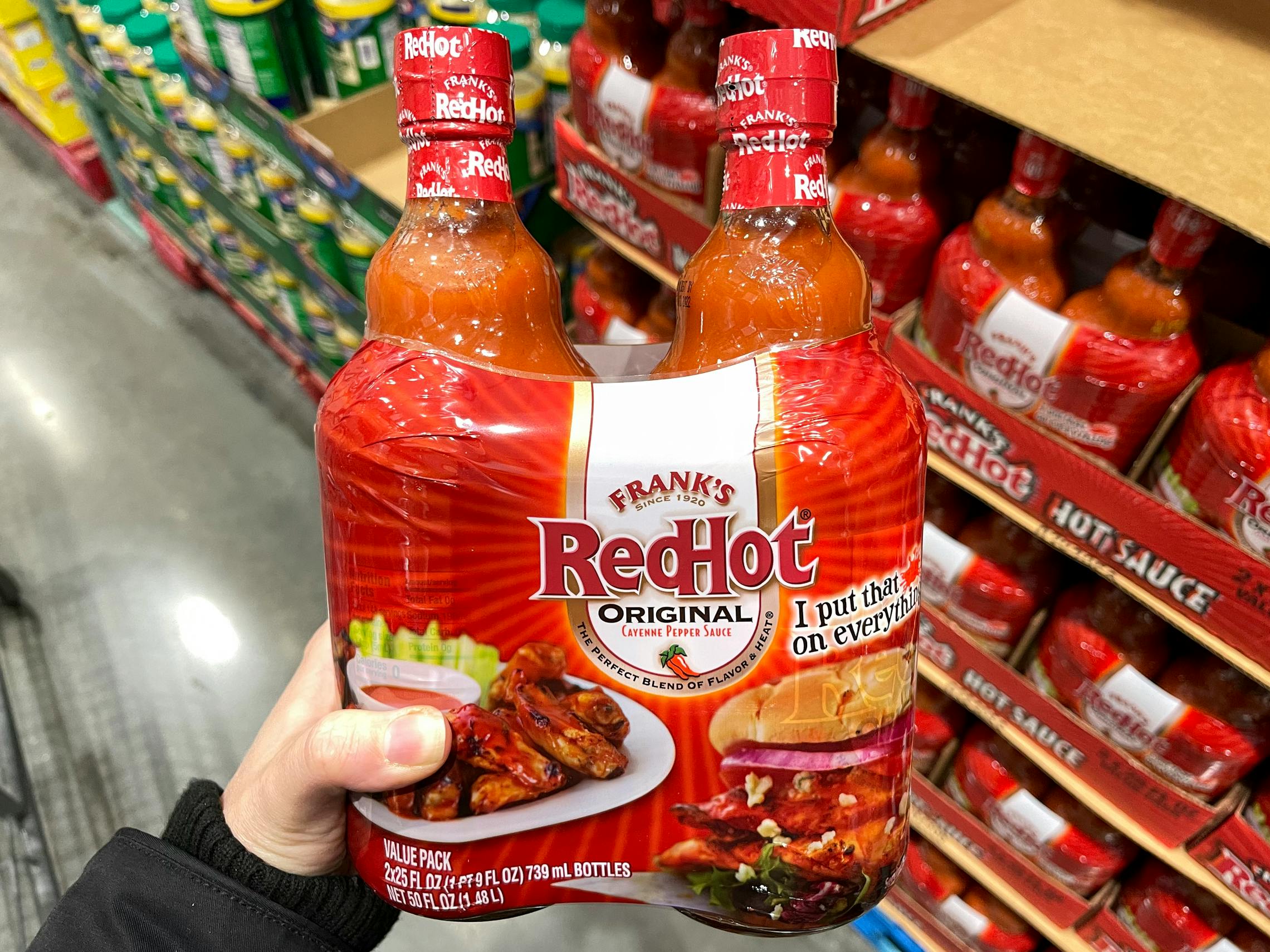 A person holding Franks RedHot sauce inside Costco