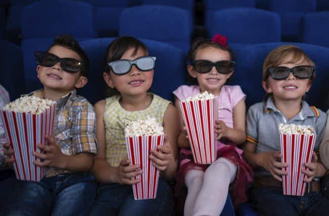 A group of children with 3D glasses on sitting while they each hold containers of popcorn.