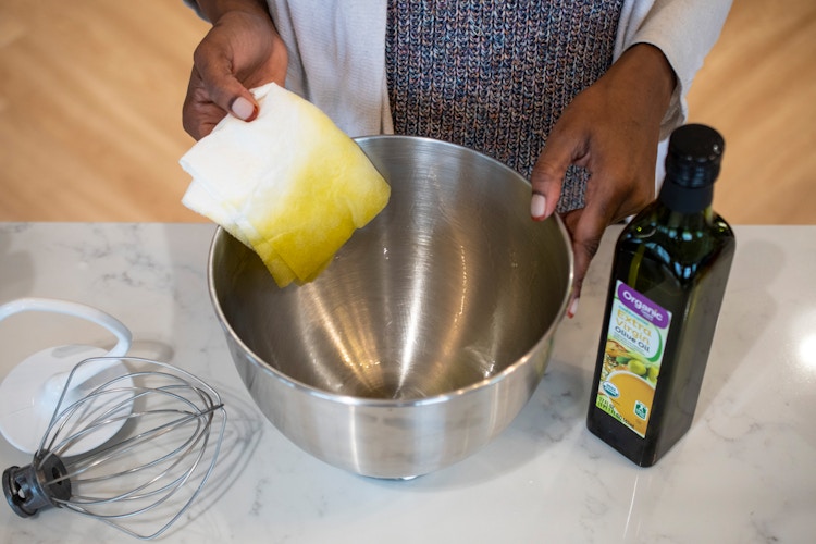 A person wiping olive oil out of a KitchenAid mixer bowl