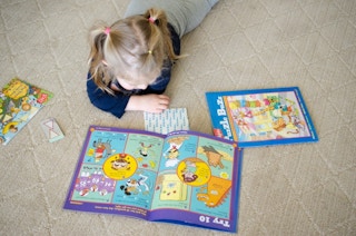 Small child laying on her stomach looking at puzzle buzz books.