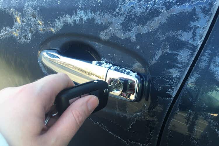 A person putting a key in a car door, covered in frost.