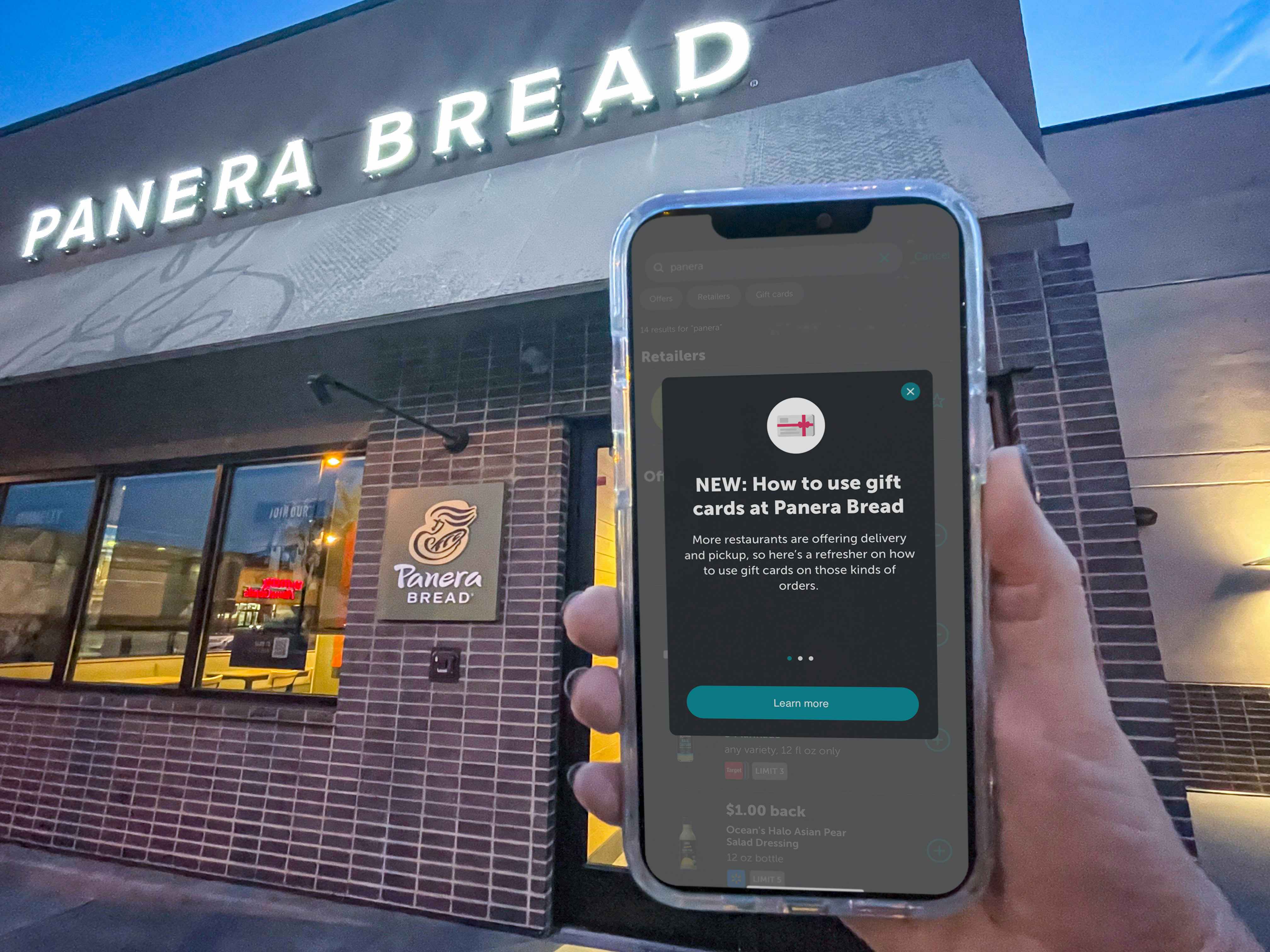 a person holding a phone up in front of a panera bread sign