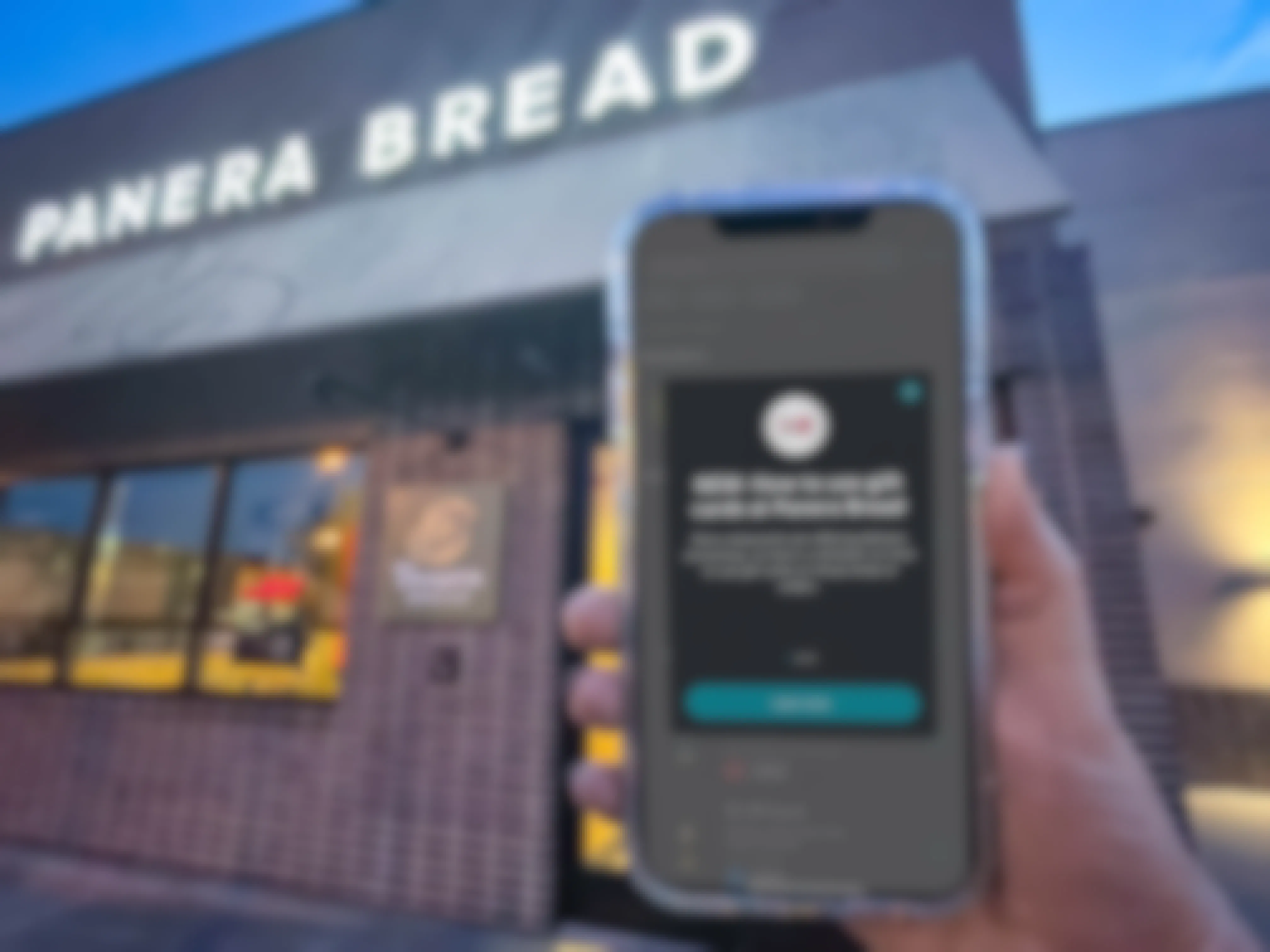 a person holding a phone up in front of a panera bread sign