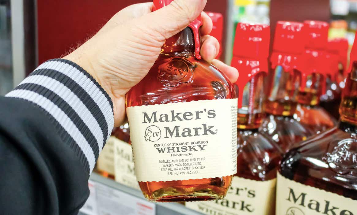 Man holding bottle of Maker's Mark whiskey in a grocery store.