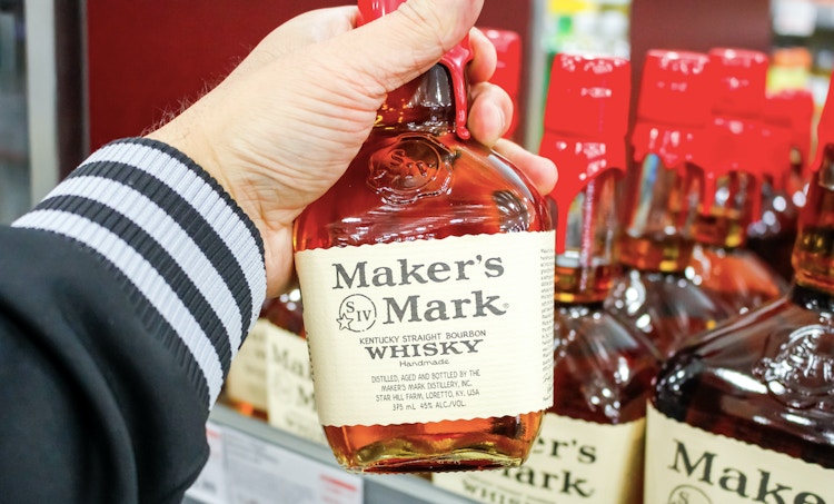 Man holding bottle of Maker's Mark whiskey in a grocery store.