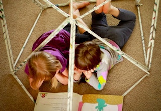 Two kids reading books inside a newspaper fort.