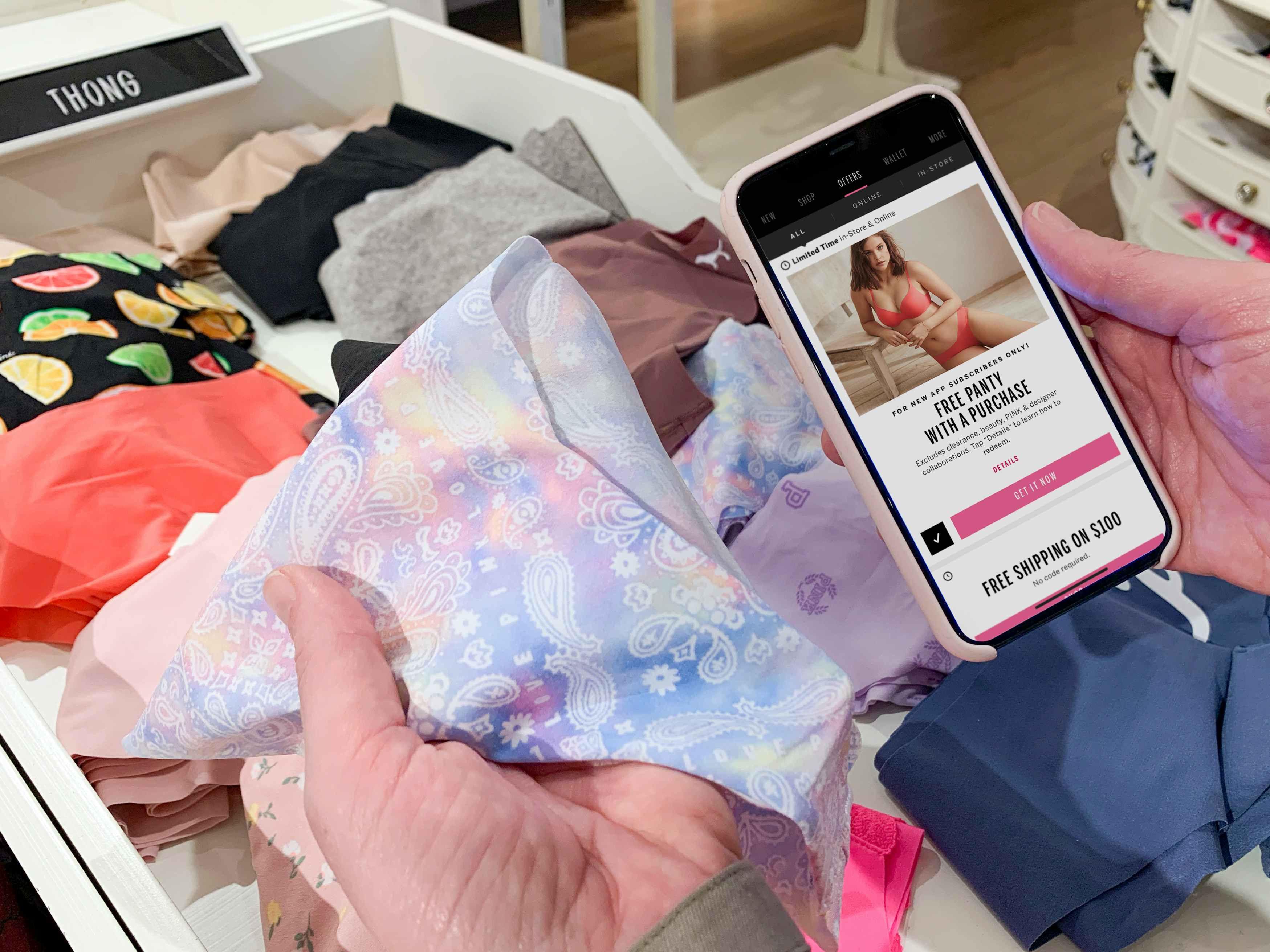 Woman holding phone with Free panty with purchase promo displayed on it, next to panties.
