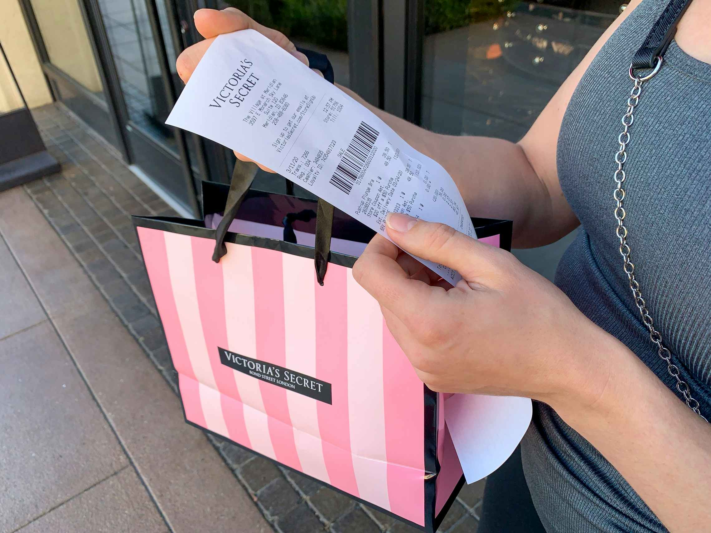 Woman looking at a Victoria's Secret receipt with shopping bag in hand.