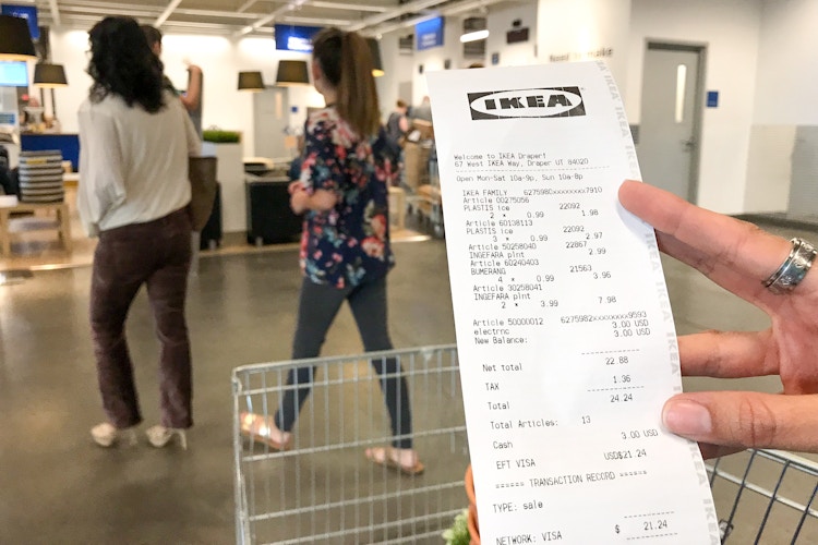 someone holding a costco receipt in front of a cart