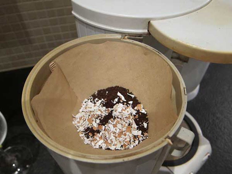 A coffee filter with ground coffee and crushed eggshells in it.
