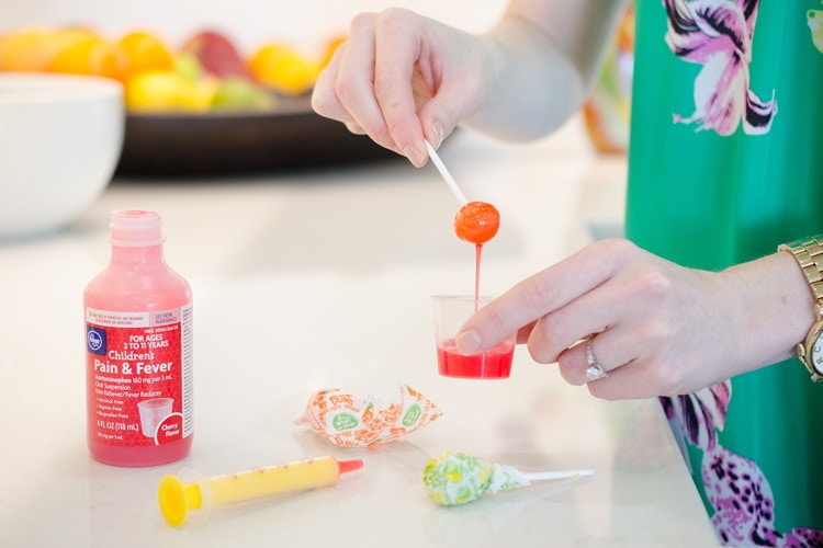 person dipping dum dum lollipop into liquid medication