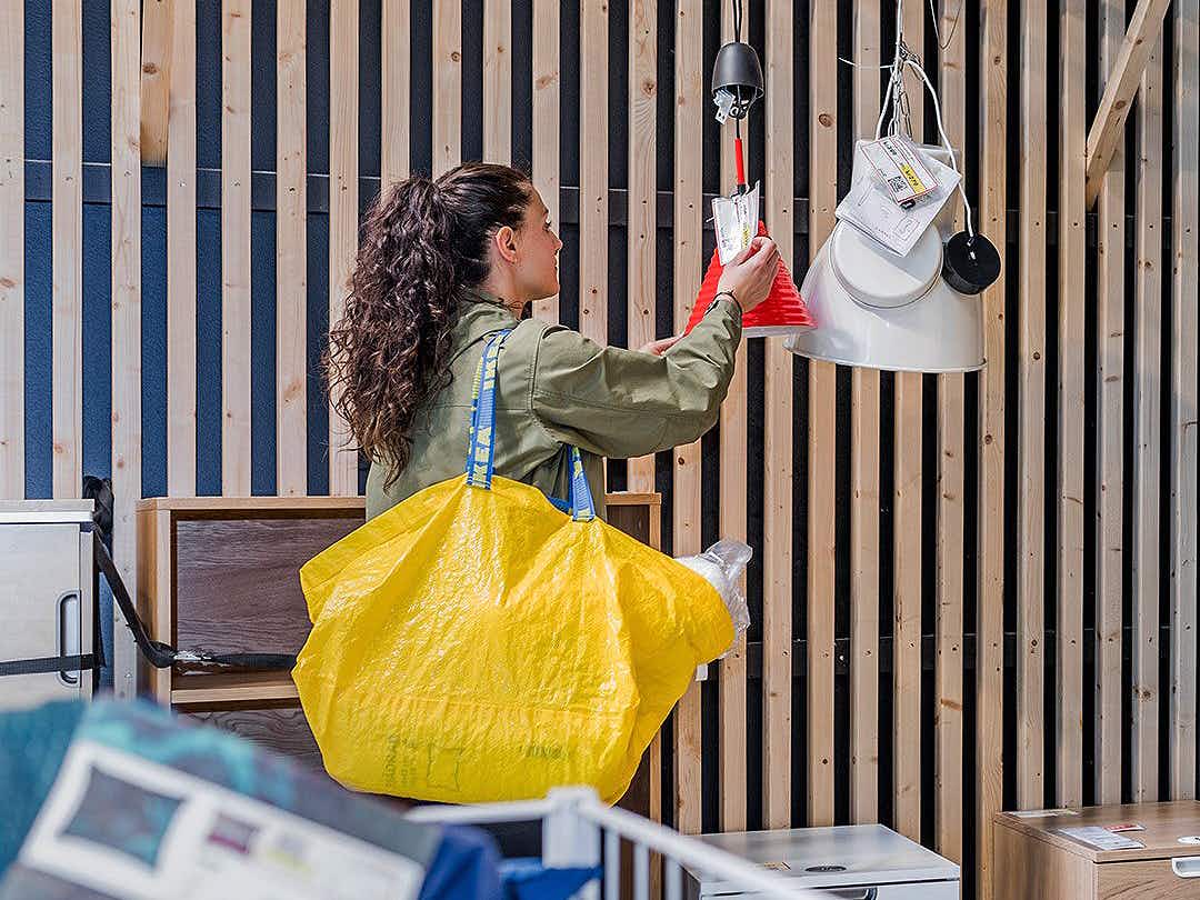 person holding a yellow ikea shopping bag and looking at pendant lamps in the store