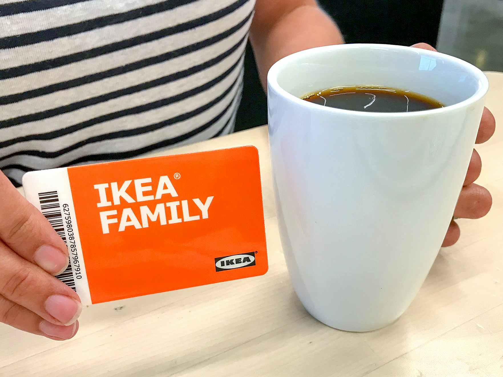 person holding an IKEA Family card next to a mug of coffee