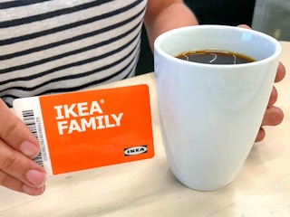 person holding an IKEA Family card next to a mug of coffee