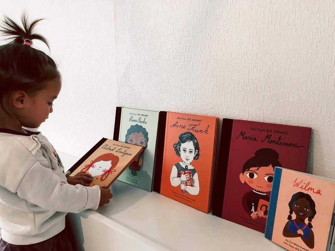 A child looking at some kids books sitting on a shelf.