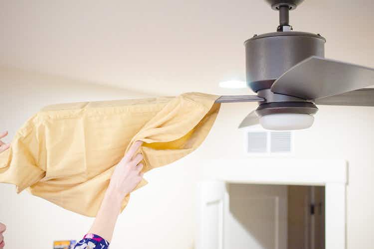 someone using a pillowcase to dust a ceiling fan blade