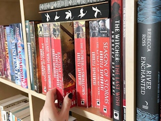 a person reaching for a book on a book shelf