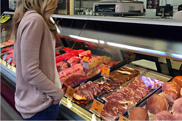 A woman looking at meat in the case at a grocery store.