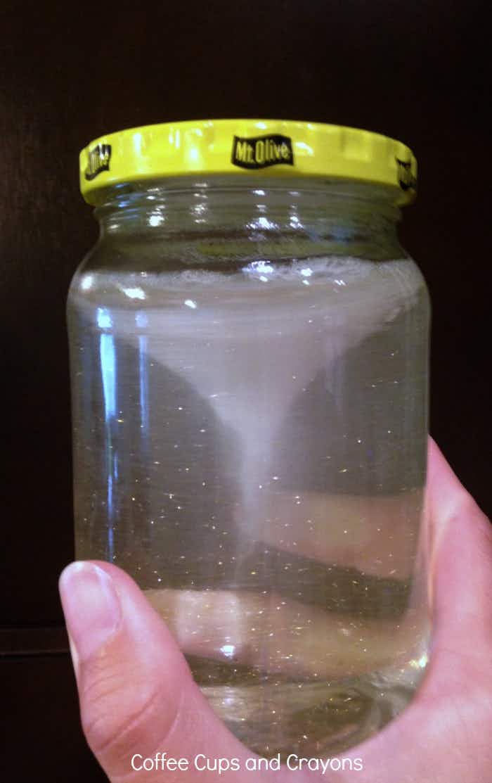 a pickle jar being held that is filled with glitter and water to make a tornado