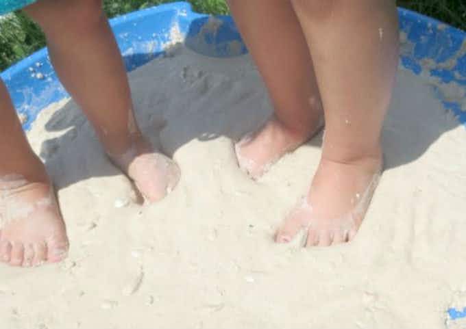 Combined cornstarch and water to make quicksand in a kiddie pool with two kids feet in the sand